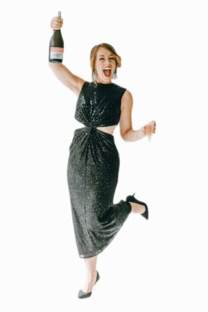 Gif of Marisol in black sparkle dress holding champaign bottle up in celebration and glass in other hand